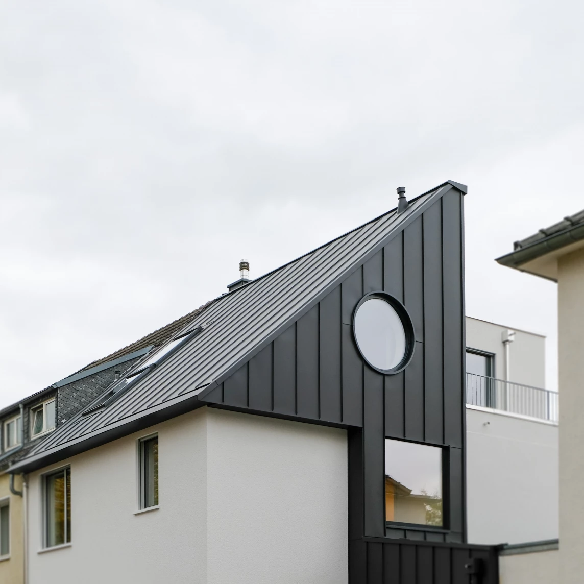 Moderner Wohnhausbereich mit schwarzer Fassadenverkleidung und runder Fensteröffnung.