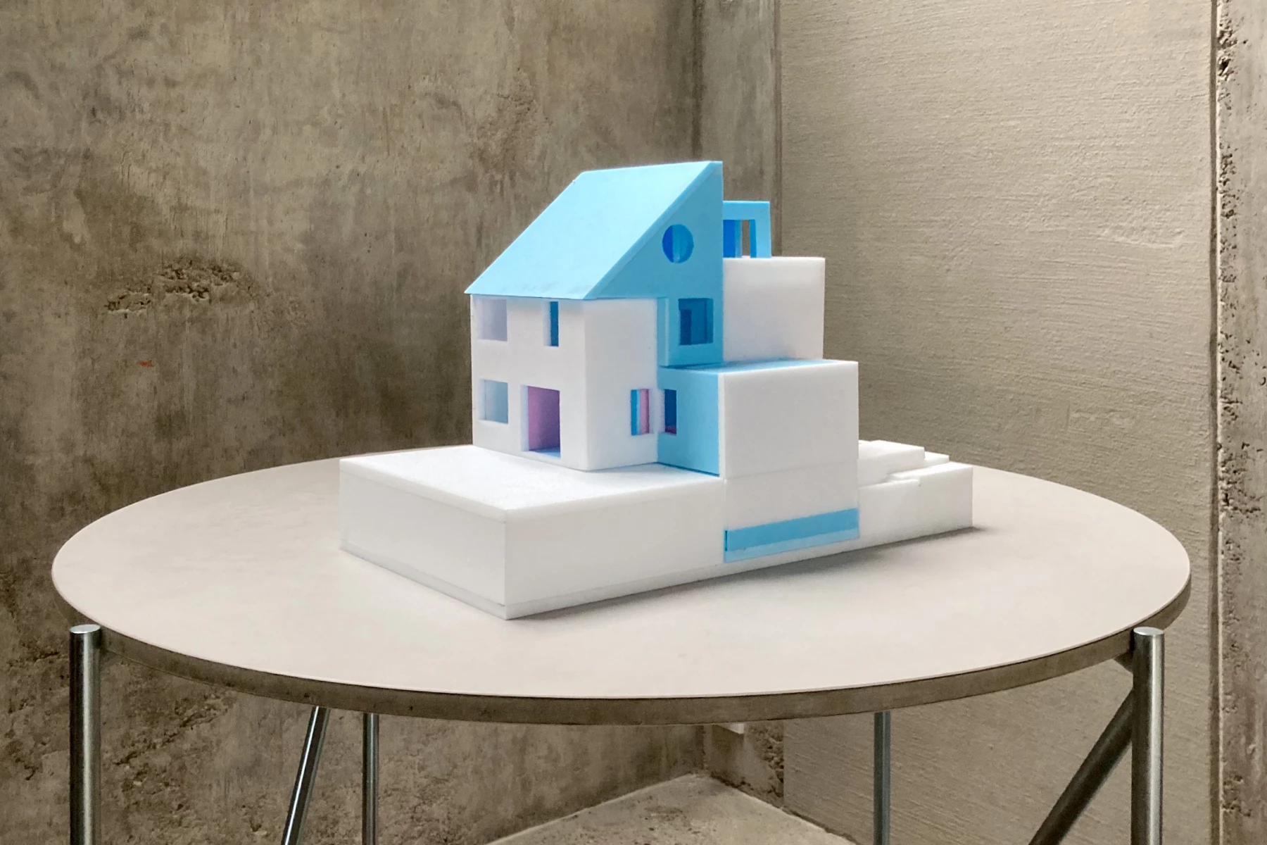 Ein Architekturmodell eines modernen Hauses mit blauen und weißen Elementen auf einem runden Tisch.